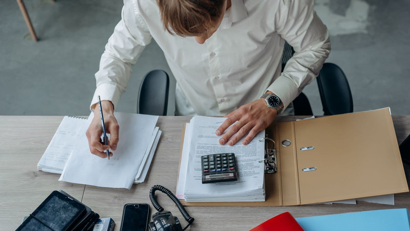 Un homme vérifie des documents dans un classeur avec une calculatrice et prend des notes à son bureau