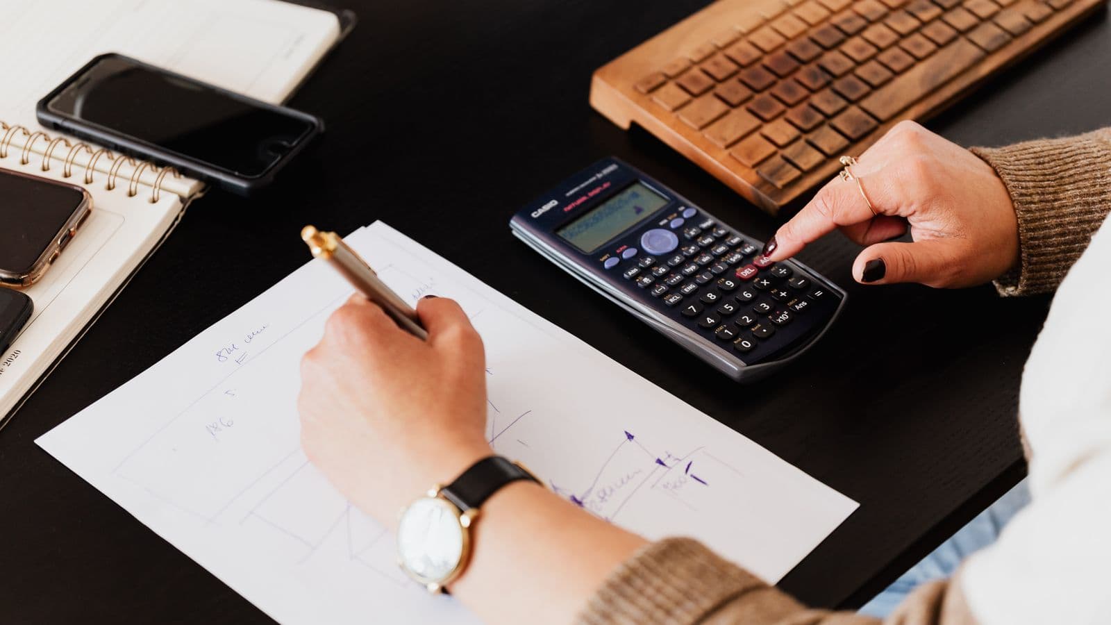 Une main calcule à la calculatrice pendant que l'autre prend des notes