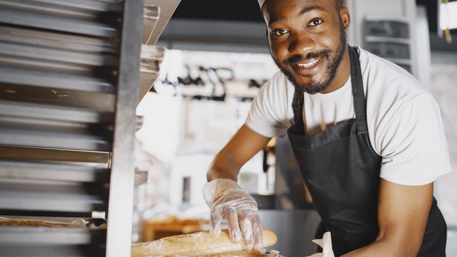 Un boulanger souriant sort des baguettes d'une étagère de cuisson dans son fournil